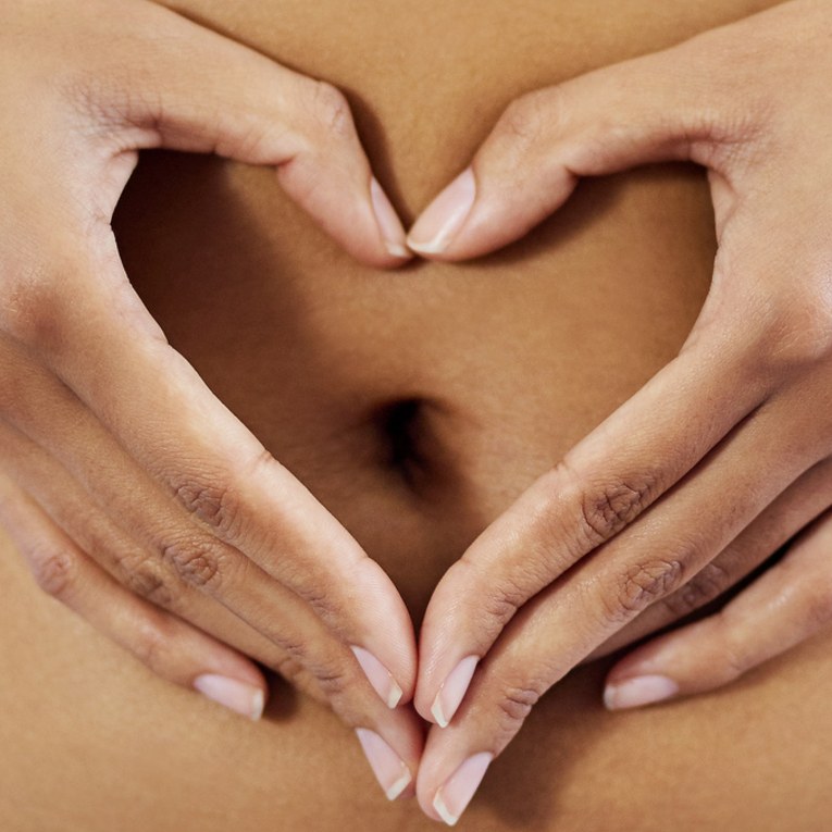 Hands forming a heart shape over a woman’s stomach